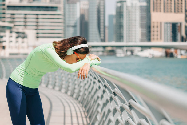 Žena trpící dušností nebo astmatem se opírá o plot a odpočívá po běžícím cvičení na nábřeží Dubai Marina - Fotografie, Obrázek