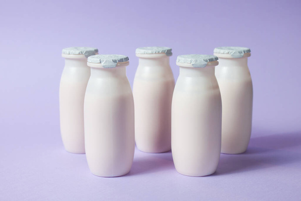 Bottles with probiotics and prebiotics dairy drink on light purple background. Bio yogurt with useful microorganisms. Production with biologically active additives. Fermentation and diet healthy food. - Фото, зображення