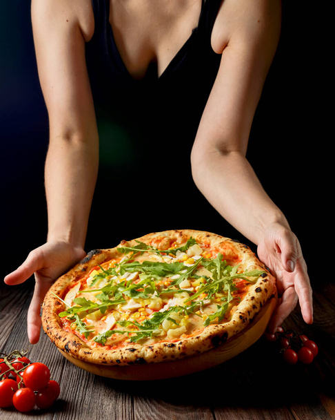 Tasty pizza on a black background with spices and vegetables. Womans hand reaching for pizza. Italian cuisine concept. Vertical banner. - Fotografie, Obrázek