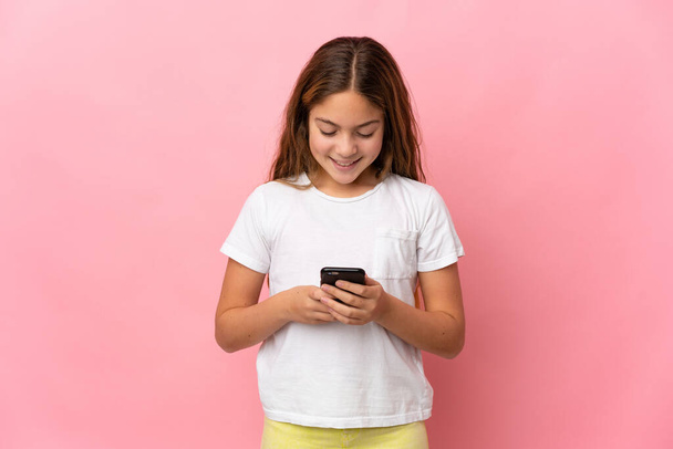 Kind over geïsoleerde roze achtergrond verzenden van een bericht of e-mail met de mobiele - Foto, afbeelding