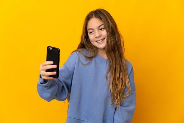 Child over isolated yellow background making a selfie - Photo, Image
