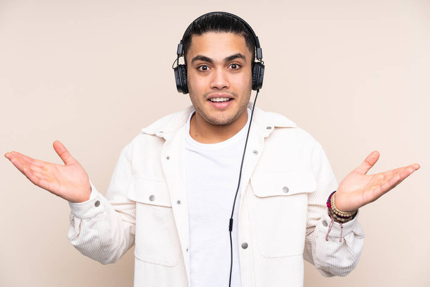 Asian handsome man isolated on beige background surprised and listening music - Photo, image