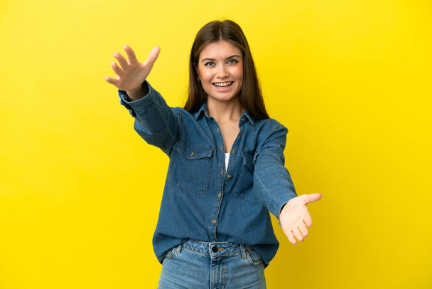 Young caucasian woman isolated on yellow background presenting and inviting to come with hand - Valokuva, kuva