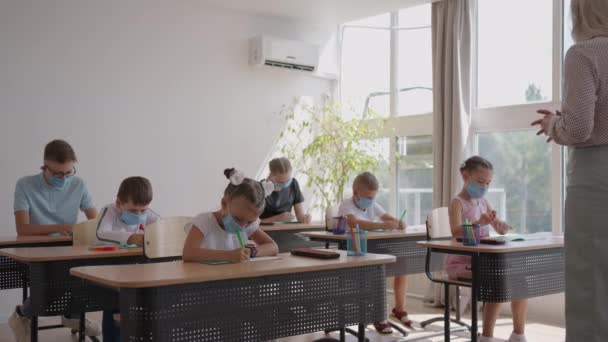 Eine multiethnische Gruppe von Kindern mit Mundschutz arbeitet in der Klasse, schreibt und hört Erklärungen des Lehrers im Klassenzimmer - Filmmaterial, Video