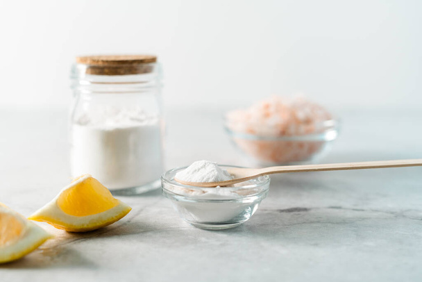 Eco friendly natural cleaners, jar with baking soda, lemon, pink salt and wooden spoon on marble table background. Organic ingredients for homemade cleaning. Zero waste concept - Photo, Image