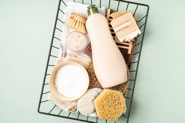 Eco friendly natural cleaners. Basket with baking soda, dish brush, soap, sponge on green background. Organic ingredients for homemade cleaning with mockup bottle. Top view Zero waste concept. - Фото, изображение