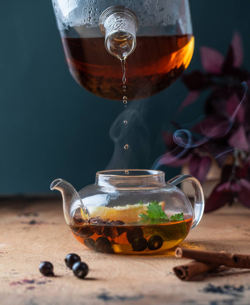 A teapot with black tea with currant berries, lemon, a cinnamon stick. Autumn background.  - Fotó, kép