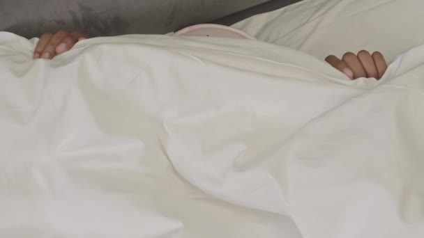 close-up van gelukkige jonge zwarte vrouw met Afrikaanse vlechten dragen slaapmasker op haar voorhoofd nemen witte deken van haar gezicht wakker in de ochtend en glimlachen naar camera - Video