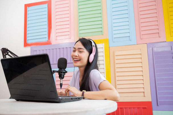 a woman using a laptop and wearing headphones while speaking in front of a microphone - Foto, Imagem