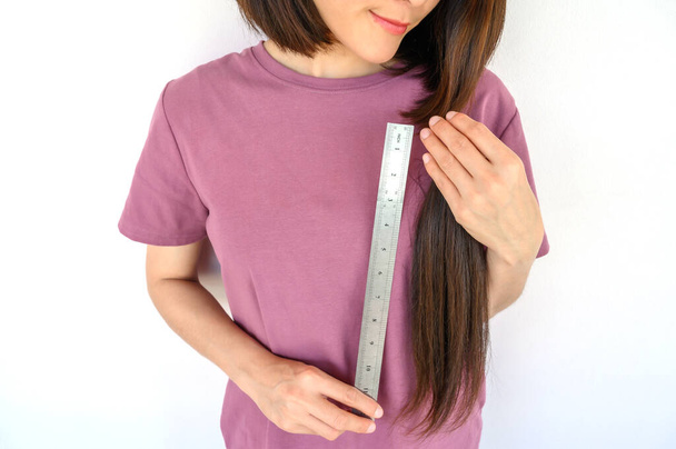 Portrait d'une femme asiatique séduisante mesurant ses cheveux avant de les couper pour don. Les cheveux utilisables peuvent transformer vos longues serrures en perruques gratuites ou à faible coût pour les personnes atteintes de cancer. - Photo, image