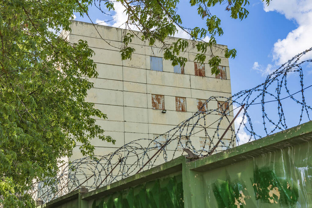 Edificio prigione di pietra, recinzione verde e filo spinato contro il cielo blu con le nuvole - Foto, immagini