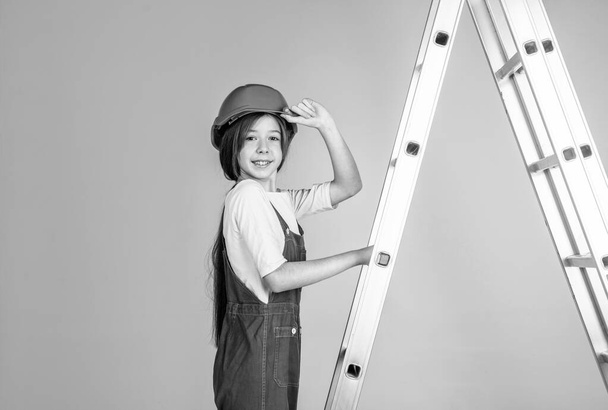 teen girl in uniform and helmet with ladder. female builder in hard hat. - Photo, Image