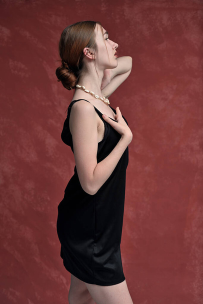 Slim model in black dress in studio posing sideways on pink background - Fotó, kép