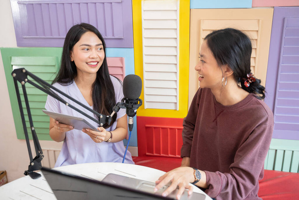 an asian girl using a tablet while chatting with her friend using a laptop in front of a microphone - Foto, Bild