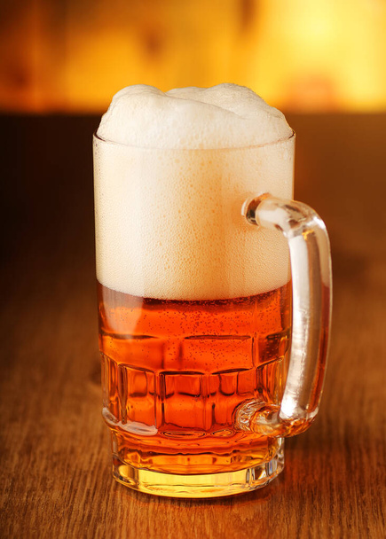 glass mug full of beer with foam on a background of wooden boards - Foto, immagini