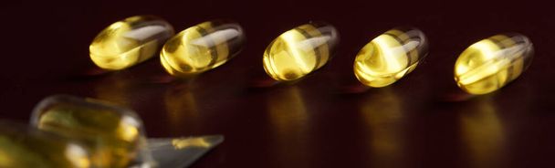 Medical transparent bright yellow capsules lie on a dark burgundy surface next to the blister. Vitamin D and prevention of viral diseases. Web banner. Selective focusing. Macro - Fotoğraf, Görsel