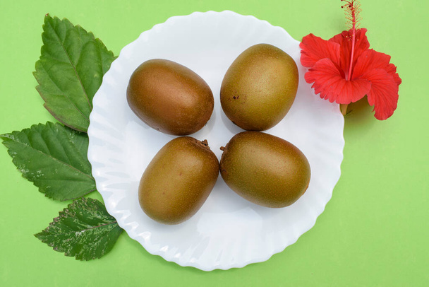 Kiwifruit сладкие дубильные фрукты считаются Суперпищей с питательными веществами. Свежие органические фрукты киви на белой тарелке с зеленым покрытием украшены цветами. - Фото, изображение