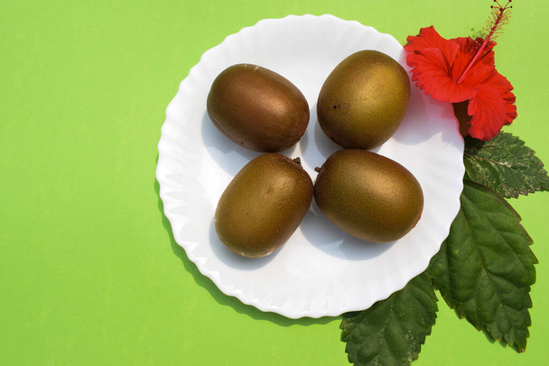 Kiwifruit сладкие дубильные фрукты считаются Суперпищей с питательными веществами. Органические плоды киви на белой тарелке с зеленым луком, украшенным цветами. Пустое место для написания текста шрифта brichure - Фото, изображение