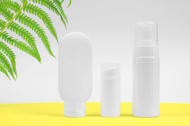 Sunscreen advertising. White tubes for cream on a yellow-white background with a leaf of a palm tree. Summer vacation and sun protection concept - Photo, Image