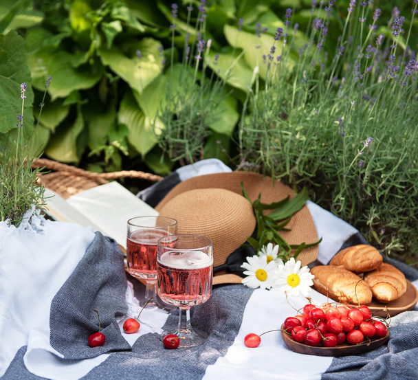 Picnic de verano en el campo de lavanda. Bodegón de verano picnic al aire libre con bayas, sombrero de paja y vino - Foto, Imagen