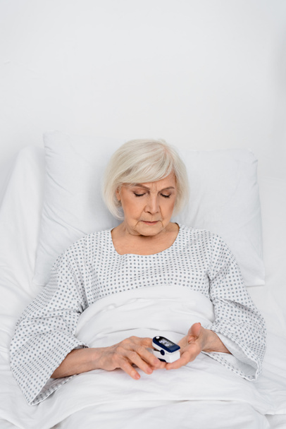 病棟のベッドで酸素濃度計を使う高齢患者   - 写真・画像