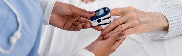 Vue recadrée de l'infirmière afro-américaine fixant l'oxymètre numérique sur la main du patient âgé, bannière  - Photo, image
