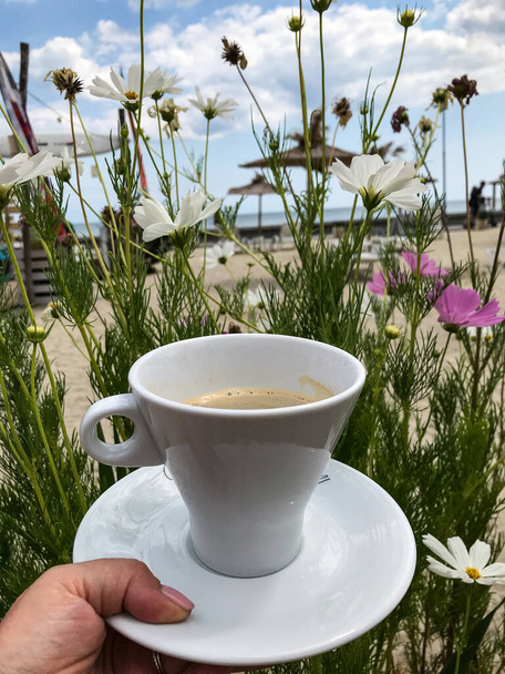 a cup of coffee in a womans hand on a background of flowers. sky and sea - Foto, Imagem