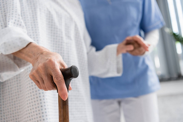 Widok starszego pacjenta trzymającego laskę w pobliżu niewyraźnej pielęgniarki  - Zdjęcie, obraz