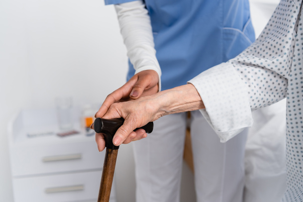 Cropped view of african american nurse and senior patient holding walking cane  - Photo, Image