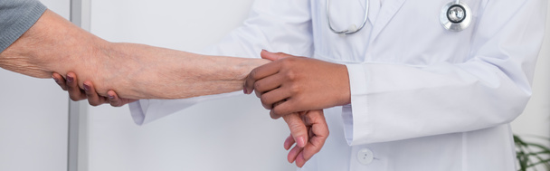 Vue recadrée du médecin afro-américain tenant la main blessée du patient âgé, bannière  - Photo, image