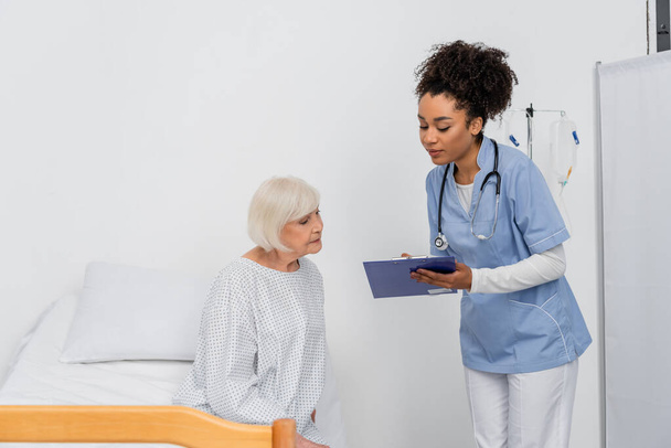 African american nurse with clipboard standing near patient in gown  - Photo, Image