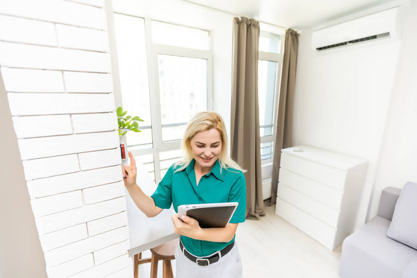 mujer que regula la temperatura de calefacción con un termostato inalámbrico moderno instalado en la pared blanca en casa. Concepto de regulación inteligente de calefacción doméstica - Foto, imagen