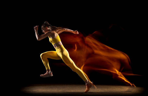 Молода жінка, спортсменка тренується ізольовано на чорному студійному фоні в змішаних неонових вогнях. Вид збоку
 - Фото, зображення