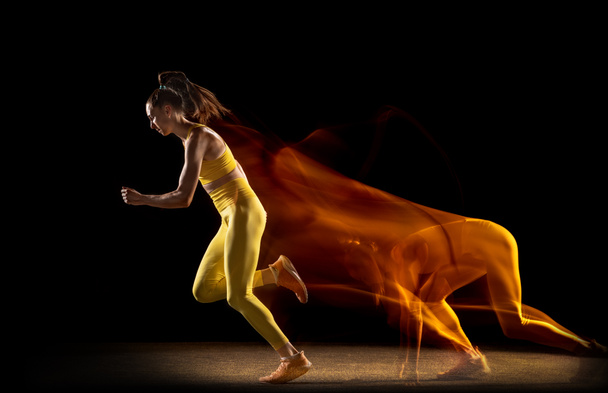 Jonge vrouw, vrouwelijke atleet in beweging, actie geïsoleerd over zwarte studio achtergrond in gemengde neon lichten. Zijaanzicht - Foto, afbeelding