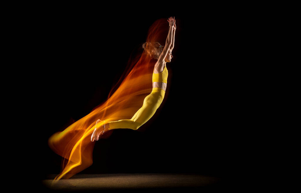 Mujer joven, atleta profesional en movimiento, acción aislada sobre fondo de estudio negro en luces de neón mixtas. - Foto, imagen