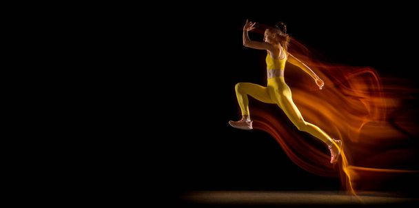 Flyer. Junge Frau, Athletin, die isoliert vor schwarzem Studiohintergrund in gemischten Neonlichtern trainiert. Seitenansicht - Foto, Bild