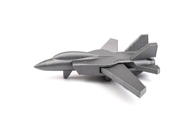 Modell eines grauen Miniatur-Kampfjets auf einem 3D-Drucker, auf weißem Hintergrund. Verkehrskonzept - Foto, Bild