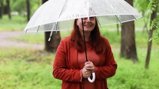 Mooie gelukkige vrouw met transparante paraplu buiten in de regen. Regendruppels. - Video