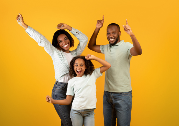 Überglückliche afrikanisch-amerikanische Dreierfamilie tanzt und genießt gemeinsam Lieblingsmusik auf gelbem Studiohintergrund - Foto, Bild