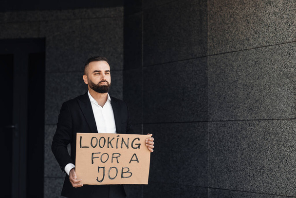 Ongelukkig wanhopige zakenman verloren werk bedrijf op zoek naar een baan placard, staan in de buurt van business center, vrije ruimte - Foto, afbeelding
