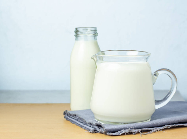 Reine Milchgetränke in klaren Gläsern und Flaschen sind natürlich gesunde Lebensmittel, die auf ein graues Tuch auf blauem Hintergrund gelegt werden..  - Foto, Bild