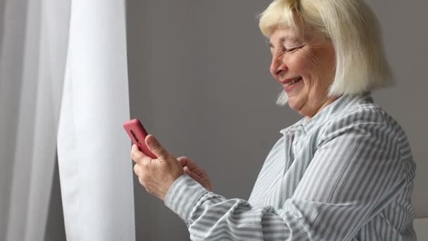 Blanc belle femme sénior textos sur téléphone mobile en utilisant Internet wifi à la maison tenant téléphone cellulaire. Dispositif technologique 5G. - Séquence, vidéo