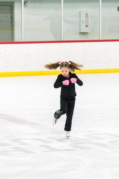 Niña practicando movimientos de patinaje artístico en la pista de hielo interior. - Foto, Imagen