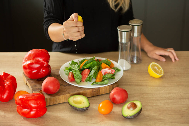 BEREIDING SALAD IN DE KEUKEN, handen knijpen citroen, tomaten, keuken, avocado - Foto, afbeelding