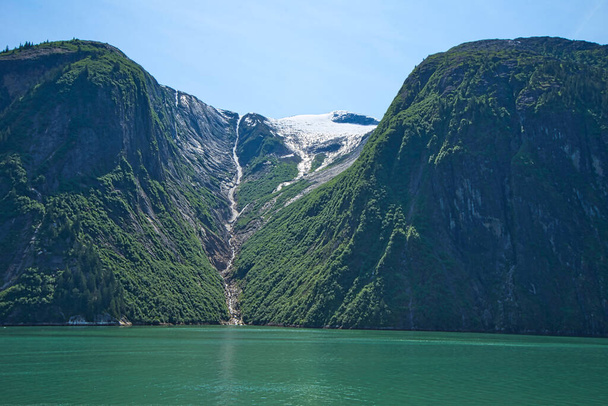 Το λιώσιμο του χιονιού σχηματίζει ένα μικρό ρυάκι που ρέει μέσα στην πράσινη λίμνη. Τα φιόρδ της Αλάσκας, μοναδικά φυσικά τοπία. Αλάσκα, ΗΠΑ. Ιούνιος 2019. - Φωτογραφία, εικόνα