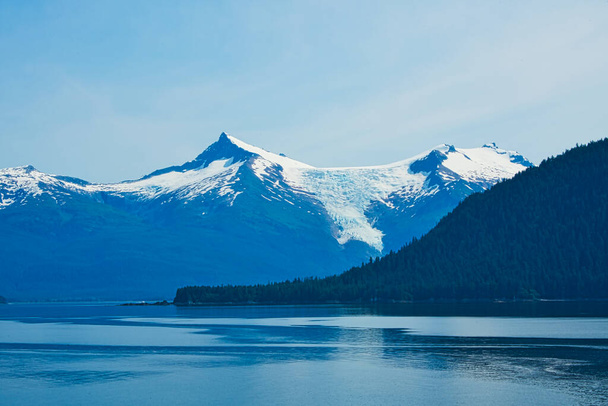 Το βουνό με τα πράσινα δέντρα. Στο βάθος είναι ένα βουνό με χιόνι. Τα φιόρδ της Αλάσκας, μοναδικά φυσικά τοπία. Αλάσκα, ΗΠΑ. Ιούνιος 2019. - Φωτογραφία, εικόνα