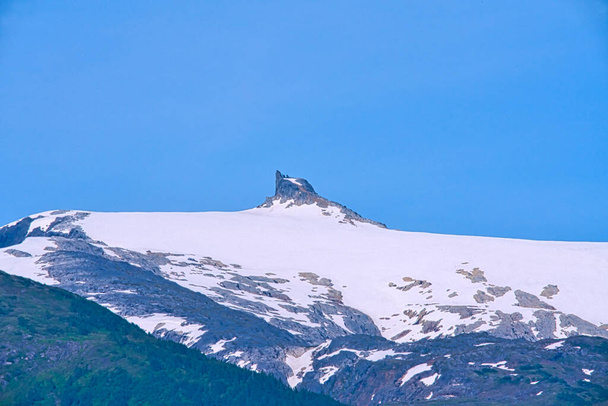 Skalisty szczyt ma kształt małego komina i otoczony jest śniegiem. Fiordy Alaski, unikalne krajobrazy przyrodnicze. Alaska, USA. czerwiec 2019. - Zdjęcie, obraz