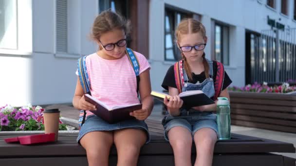  Dos chicas caucásicas lindas en gafas con mochila sentarse y leer libro - Imágenes, Vídeo