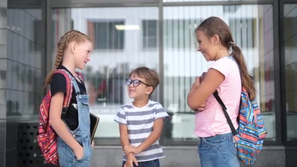 Τρία παιδιά με σακίδιο στέκονται και μιλούν μαζί και παίζουν - Πλάνα, βίντεο