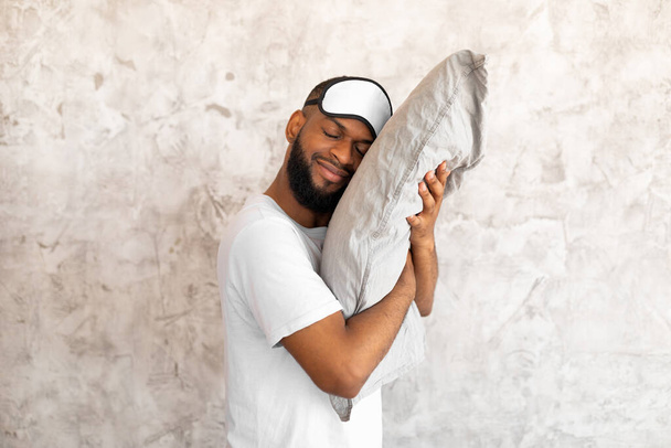 Uśmiechnięty brodaty afro facet przytulający poduszkę w domu - Zdjęcie, obraz